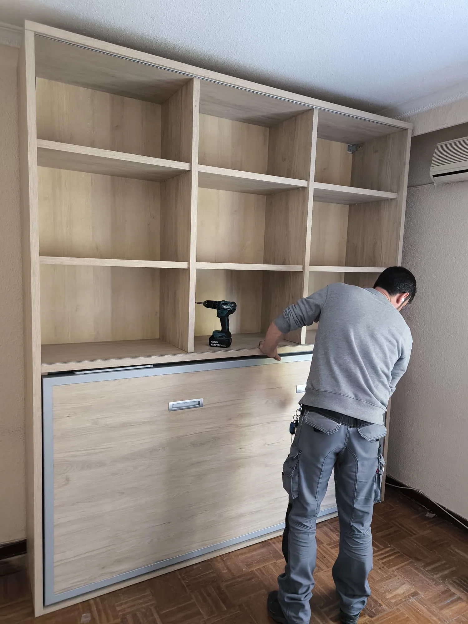 Jorge montando una cama abatible con estantería en un dormitorio